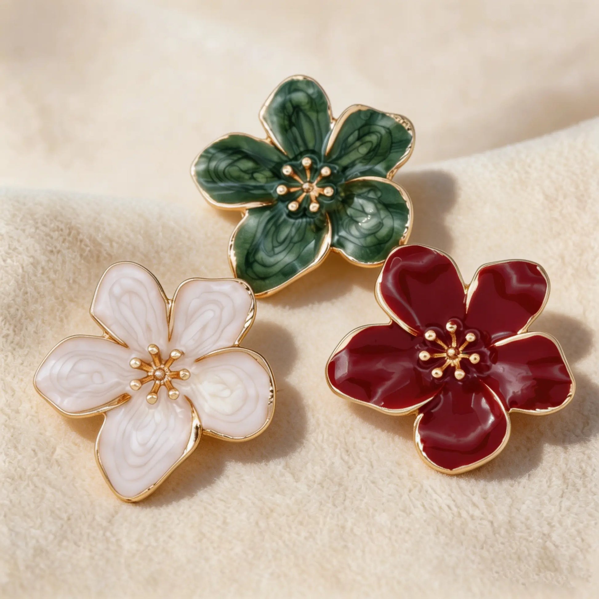 A stunning collection of three vintage-style enamel floral button covers resting on soft cream fabric under warm sunlight. Showcasing elegant color options including swirl emerald green, blush pink, and glossy burgundy red. Perfect French-style cuff accessories.