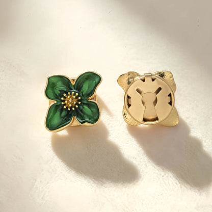 Detailed view of a vintage deep green enamel four-petal button cover resting on soft fabric under warm sunlight. The right side highlights the secure closed gold clip, demonstrating its use as an elegant French-cuff accessory.