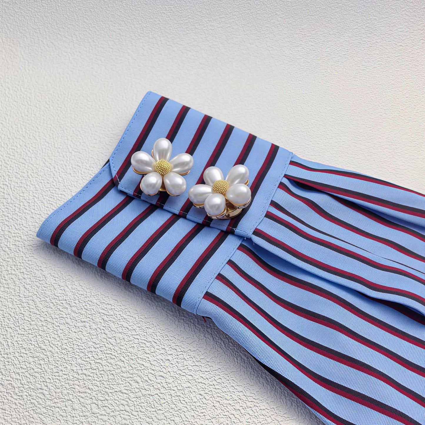 Two elegant white pearl floral button covers with textured gold centers, styled flawlessly as cuff accessories on a blue striped shirt sleeve. A perfect light luxury faux cufflink upgrade for everyday wear.