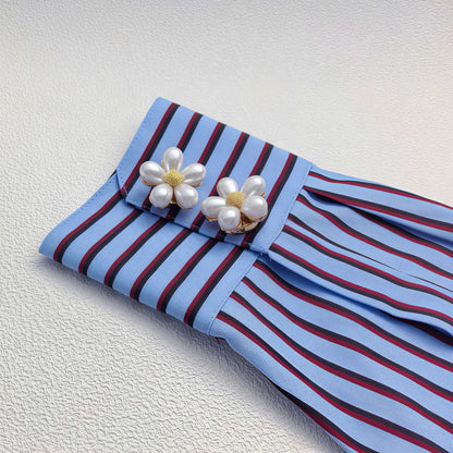 Two elegant white pearl floral button covers with textured gold centers, styled flawlessly as cuff accessories on a blue striped shirt sleeve. A perfect light luxury faux cufflink upgrade for everyday wear.